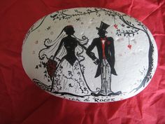 a painted rock with an image of a bride and groom holding hands on red paper