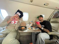 two people sitting at a table with food and drinks in front of them on an airplane