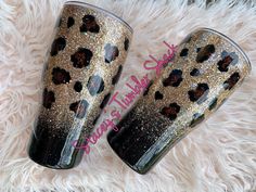 two black and gold leopard print tumblers sitting on top of a fluffy white blanket