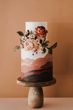 a white and pink cake with flowers on it sitting on top of a wooden stand