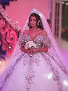 a woman in a wedding dress is walking down the runway wearing a tiara and holding a bouquet