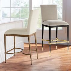 two white and gold barstools in front of a window with wood flooring