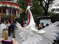 a large white bird standing on top of a sidewalk next to a crowd of people