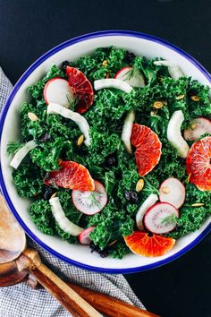 a bowl filled with kale salad and oranges on top of a wooden spoon