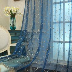 a chair sitting in front of a window covered in blue sheer curtains with white speckles