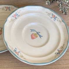 two white plates sitting on top of a wooden table next to flowers and branches in the background