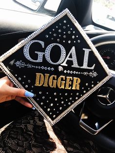 a person holding up a black and gold graduation cap that says goal digger on it