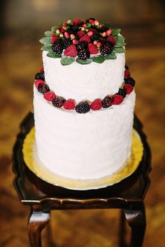 a white wedding cake with berries and leaves on top sits on a small wooden stand