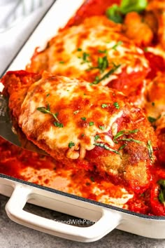 a casserole dish with meat, cheese and tomato sauce in it is being held by a spatula