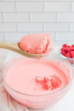 a spoon full of pink cake batter with raspberries in the bowl next to it