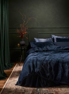 a bed with blue sheets and pillows on top of it next to a green wall