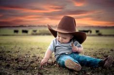 a little boy wearing a cowboy hat sitting on the ground