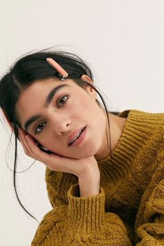 a woman with her chin resting on her hand, wearing a sweater and hair clips