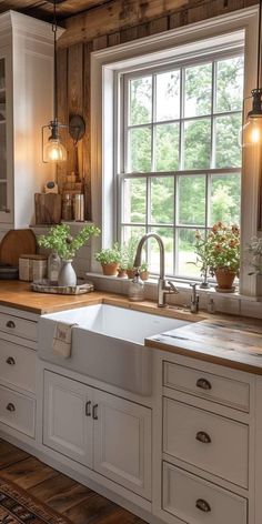 a kitchen with white cabinets and wooden floors, windows above the sink are potted plants