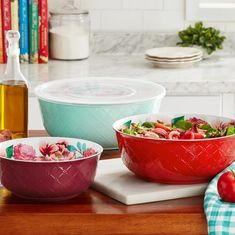 three bowls with salad in them sitting on a counter next to a bottle of olive oil