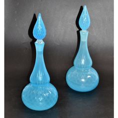 two blue glass vases sitting on top of a black table next to each other