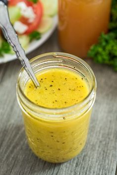 a glass jar filled with mustard sitting on top of a table next to a plate of vegetables