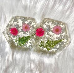 two glass trays with pink flowers and green leaves in them on a white fur surface