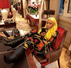 a woman sitting on top of a red chair next to two black boots and a purse