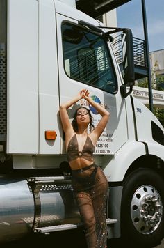 a woman in fishnet clothing standing next to a semi truck with her hands on her head