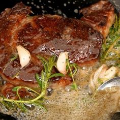 some meat is cooking in a pan with mushrooms and herbs on the side, next to a spatula