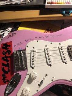 a pink electric guitar sitting on top of a desk next to a pile of books