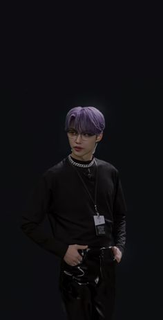 a man with purple hair and black pants standing in front of a dark background,