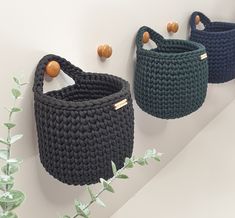 three crocheted baskets are hanging on the wall next to some green planters