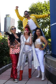 three women and one man are posing for the camera in costumes with their arms up