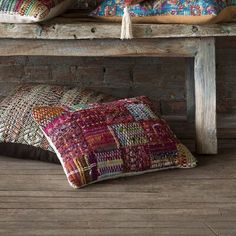 two pillows sitting on top of a wooden bench next to a brick wall and floor