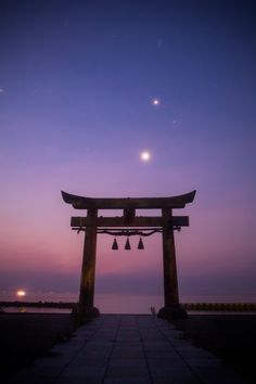 an arch with bells in front of a body of water at night, under a purple sky