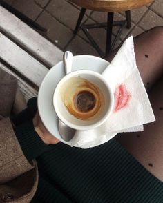 a person holding a cup of coffee on top of a white saucer and napkin