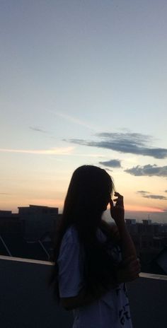 a woman standing on top of a roof talking on a cell phone while the sun is setting