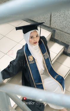 a woman in a graduation cap and gown is sitting on stairs with her hands behind her back