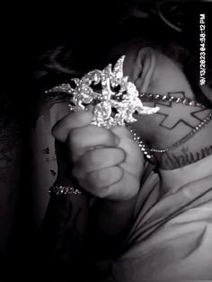 a black and white photo of a woman with tattoos on her chest holding a diamond brooch