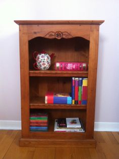 a wooden book shelf with books and a teapot on top