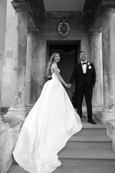 a man and woman in formal wear standing on the steps of an old building holding hands