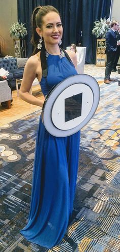 a woman in a blue dress is holding a shield and smiling at the camera while standing on a carpet