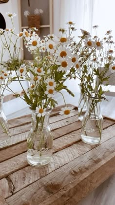 three clear vases filled with white and yellow flowers on top of a wooden table