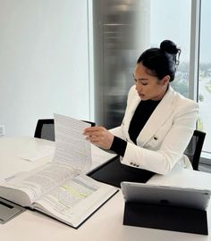 a woman sitting at a table with an open book in front of her, reading