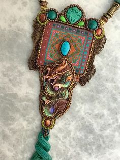 This amazing piece of wearable art is so stunning. It is a collection of various pieces coming together in balance and honoring the year of the dragon. The top has jacquard ribbon with a turquoise stone resting upon it. Above is a carved stone, chrysocolla, sun stone, and Mohave turquoise. On the sides is some vintage metal lace, and of course the main focal a hand carved and painted bone dragon. Hanging from the bottom is another pieces of carved and dyed bone. Wow what a powerful piece. This pendant measures 3 inches wide X 8 inches long and hangs from a 16 inch 4mm leather cord with a 2 inch adjustable chain. Definitly a one of a kind piece. Bone Dragon, Embroidered Jewelry, Jacquard Ribbon, Sun Stone, Bead Embroidery Jewelry, Carved Stone, Metal Lace, Year Of The Dragon, Embroidery Jewelry