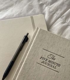 two notebooks sitting on top of each other with a pen laying next to them