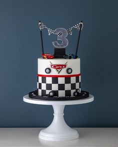 a three tiered race car cake on a white pedestal in front of a blue wall