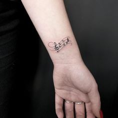 a woman's hand with a musical note tattoo on her left wrist and the word music written in cursive writing