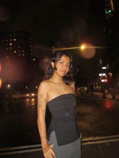 a woman standing in the street at night with her arm around her waist and tattoos on her chest