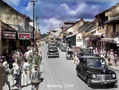 an old time photo of people walking down the street in front of cars and buildings