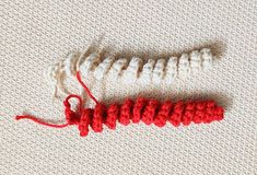 two red and white crocheted objects laying on top of a knitted surface