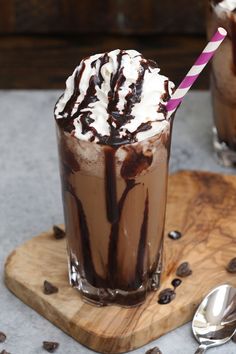 two glasses filled with chocolate milkshakes on top of a cutting board next to spoons