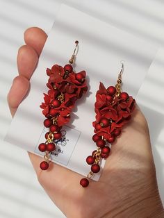 a pair of red flowers and pearls are being held by a hand