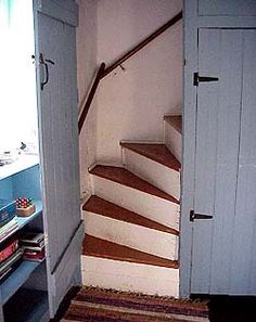 an open door leading up to a set of stairs in a room with books on the floor